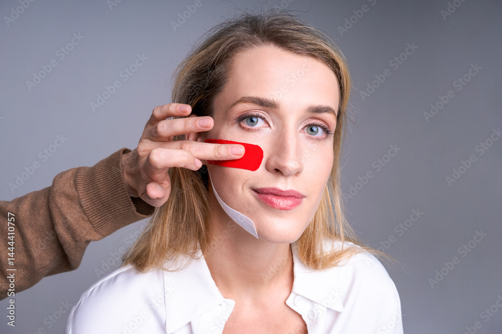 woman with tapes on her face and hands specialist measuring face contour for cosmetic procedures, skin care and aesthetic correction concept, light background.