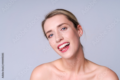 A woman in a natural look playfully winks and sticks out her tongue, conveying an atmosphere of freedom, happiness and lightness against a neutral background.