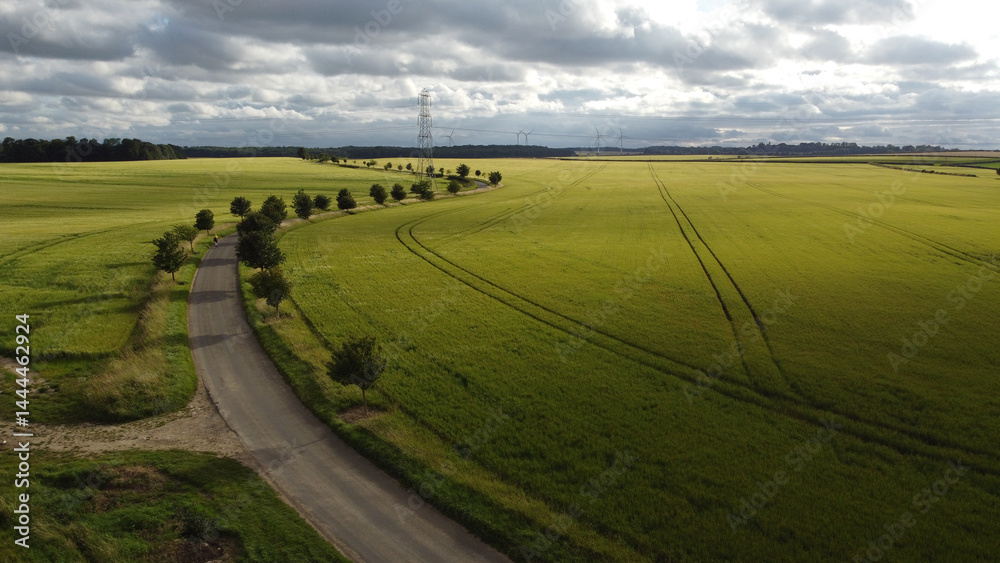 Fototapeta premium Aerial view of small rural winding road with single cyclist in distance