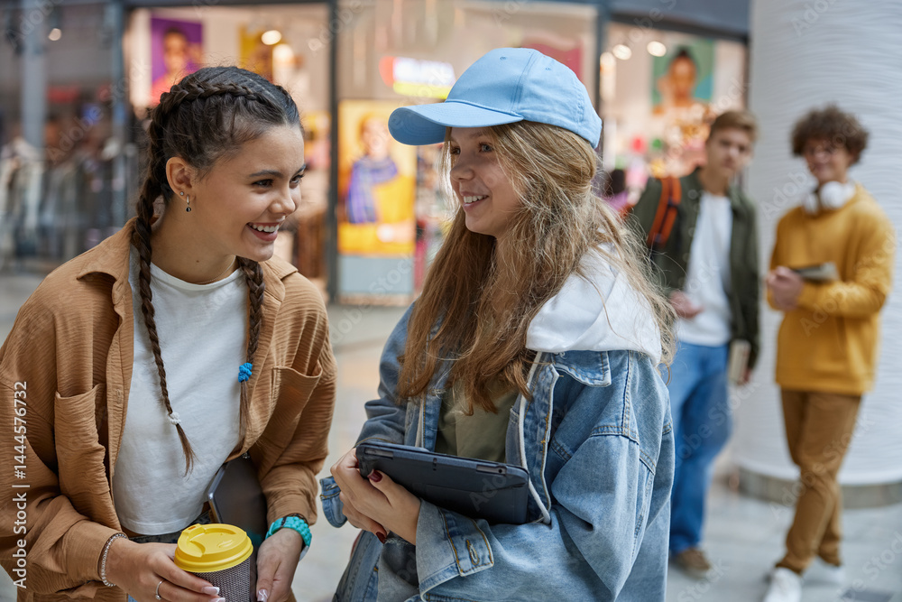 Teenage girls friends gossiping, talking and laughing together in shopping mall