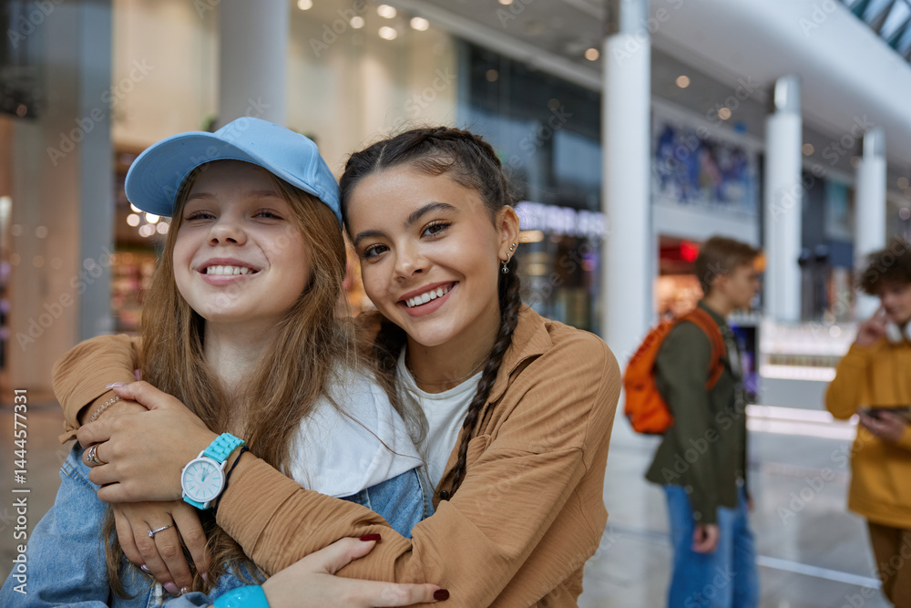 Happy teenage girls friends hugging while posing over shopping center