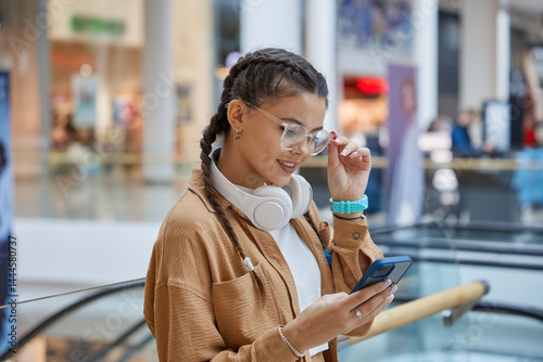 Obraz na płótnie Teenage girl using smartphone while walking over shopping mall background w salonie