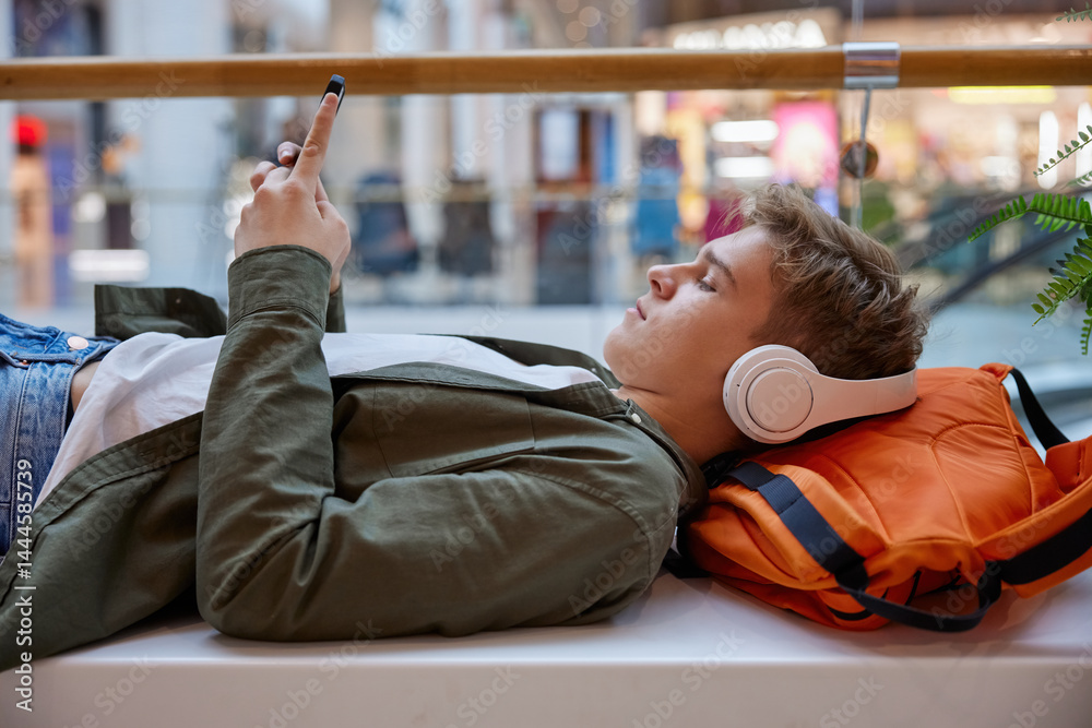 Teenage boy listening to music using smartphone resting in shopping mall