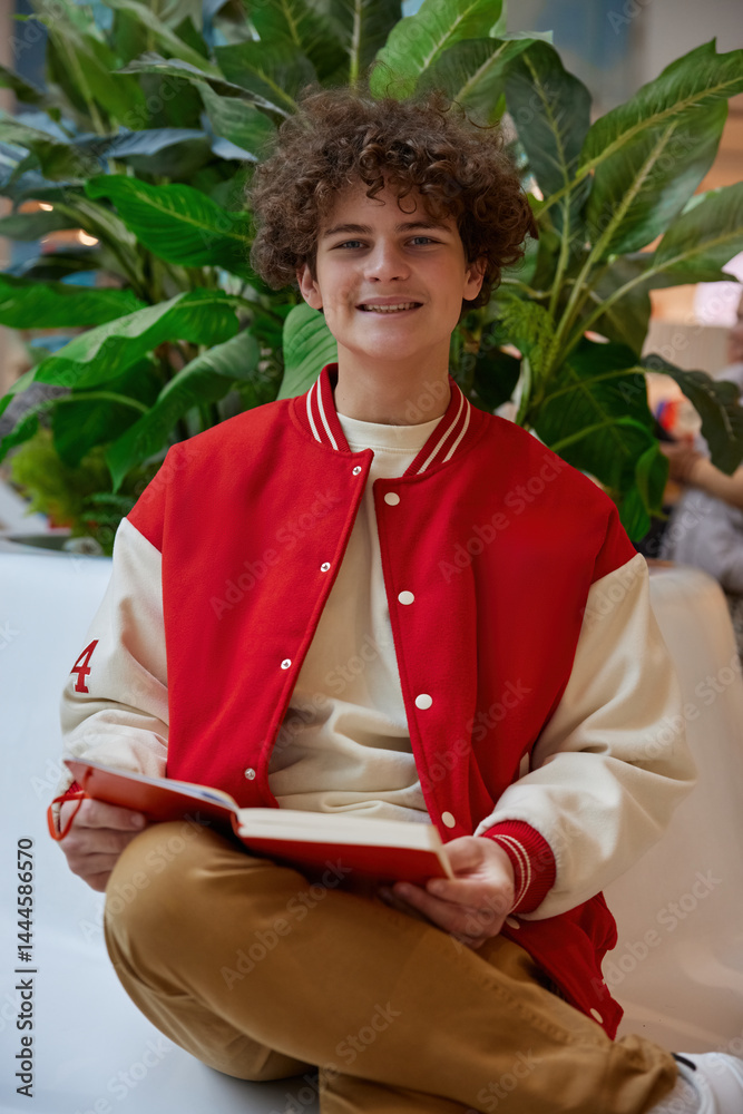 Handsome teenage boy reading book while rest in shopping mall