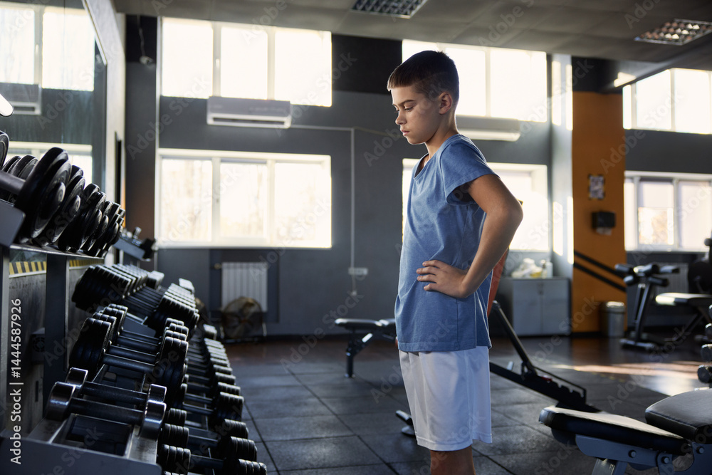 Teenage boy choosing dumbbell weight for training workout at gym
