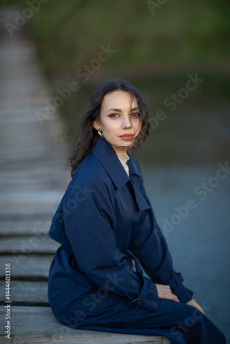beautiful brunette european girl in blue trench coat at nature. Young lady with beautiful face.