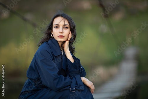 beautiful brunette european girl in blue trench coat at nature. Young lady with beautiful face.