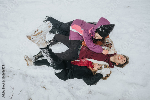Three people lie together in snow, laughing and playing in a winter wonderland, showcasing joy, bonding, and the cheerfulness of cold weather adventures among loved ones outdoors.
