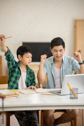 The father is teaching his son his homework with care at his home.