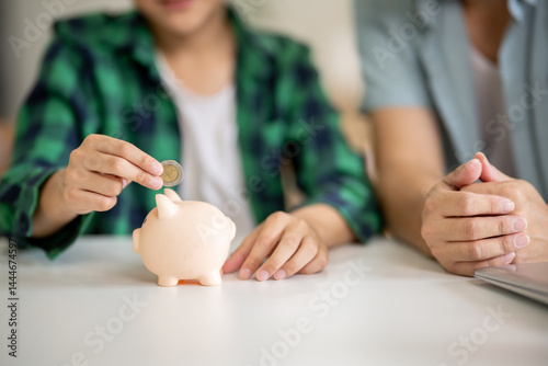 A father is teaching his son how to save money by putting money in a piggy bank.