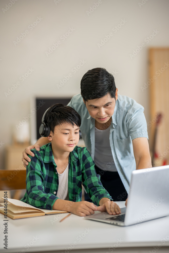 A father comes to cheer on his son while he is studying online on his laptop at home. A father comes to cheer on his son while he is studying online on his laptop at home.