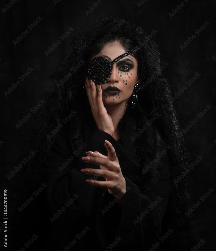 Indian female fashion model dressed in black with one eye covered. Indoor studio portrait.