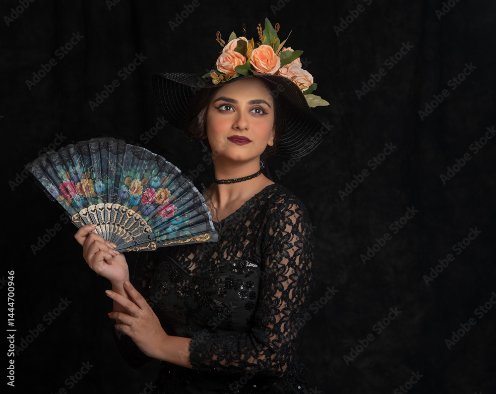 Indian female fashion model dressed in black with a floral hat. Studio portrait.