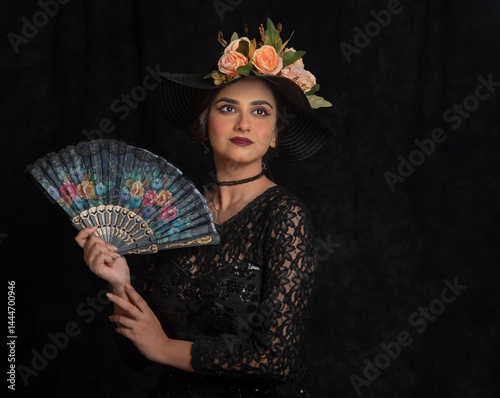 Indian female fashion model dressed in black with a floral hat. Studio portrait.