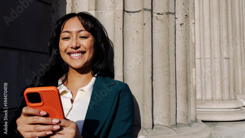 Smiling woman using smartphone outdoors near architectural columns