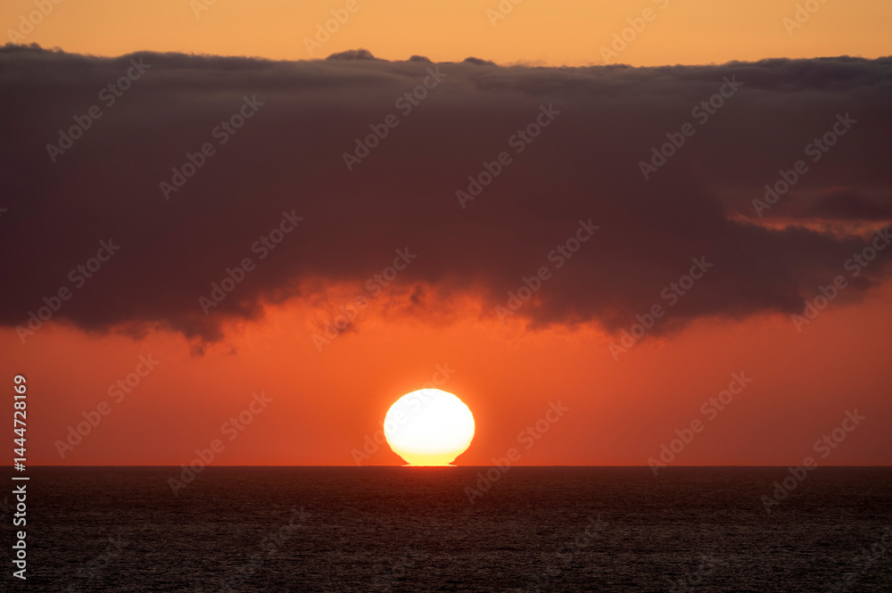 Very moody and dramatic sky over the cloudy ocean horizon, with strong orange, sunbeams and traces of lingering storm cells