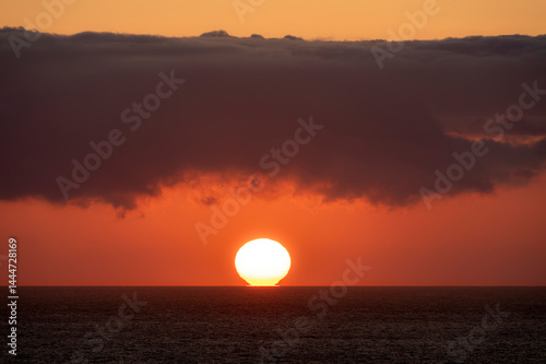 Very moody and dramatic sky over the cloudy ocean horizon, with strong orange, sunbeams and traces of lingering storm cells 