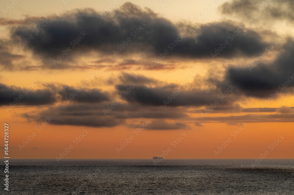 Very moody and dramatic sky over the cloudy ocean horizon, with strong orange, sunbeams and traces of lingering storm cells