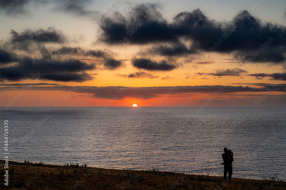 Father holds child on bluff during a dramatic sky, looking out along the coast