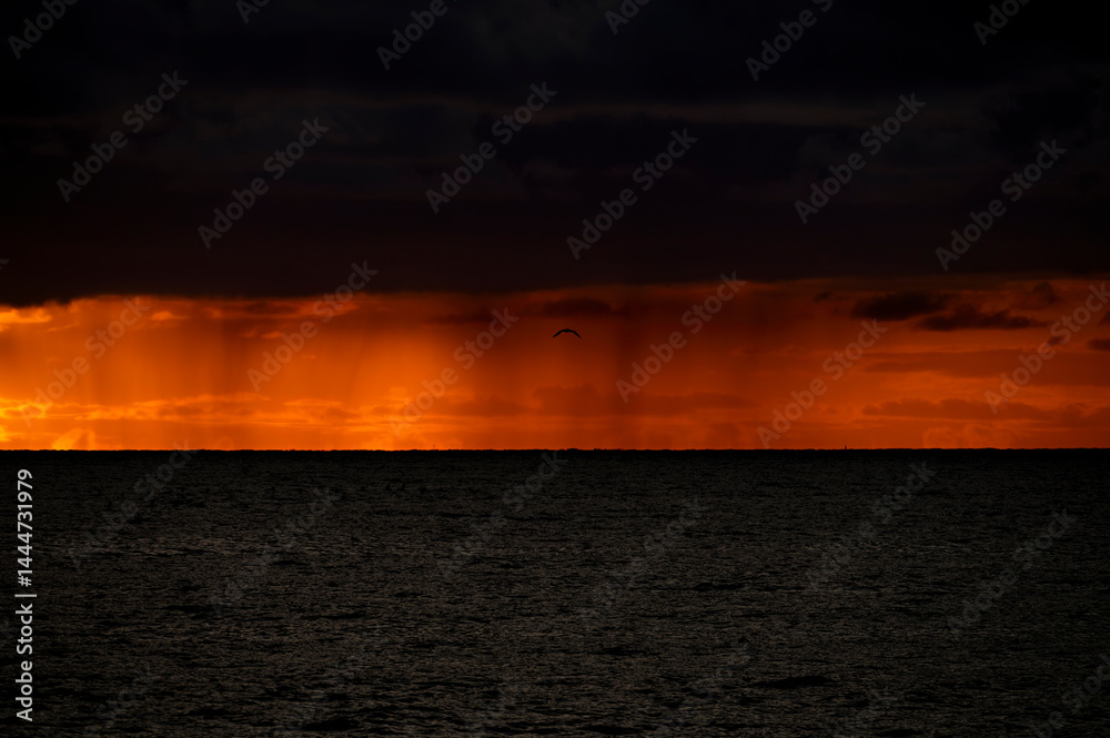 Very moody and dramatic sky over the cloudy ocean horizon, with strong orange, sunbeams and traces of lingering storm cells