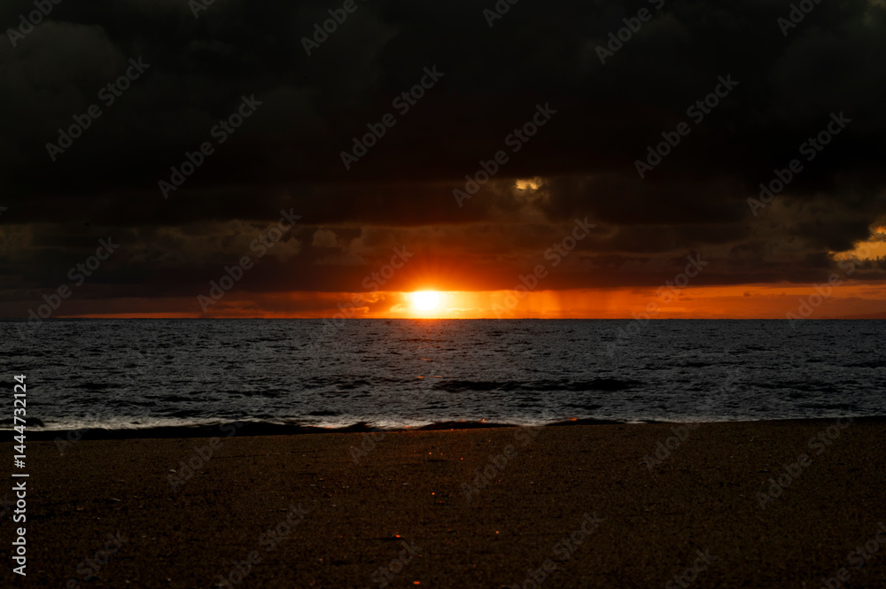 Very moody and dramatic sky over the cloudy ocean horizon, with strong orange, sunbeams and traces of lingering storm cells
