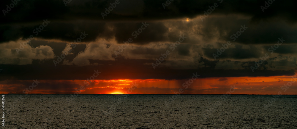 Very moody and dramatic sky over the cloudy ocean horizon, with strong orange, sunbeams and traces of lingering storm cells