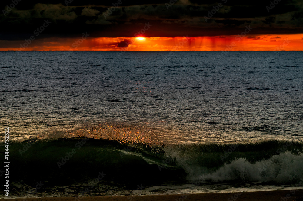 Very moody and dramatic sky over the cloudy ocean horizon, with strong orange, sunbeams and traces of lingering storm cells