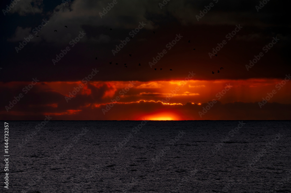 Very moody and dramatic sky over the cloudy ocean horizon, with strong orange, sunbeams and traces of lingering storm cells
