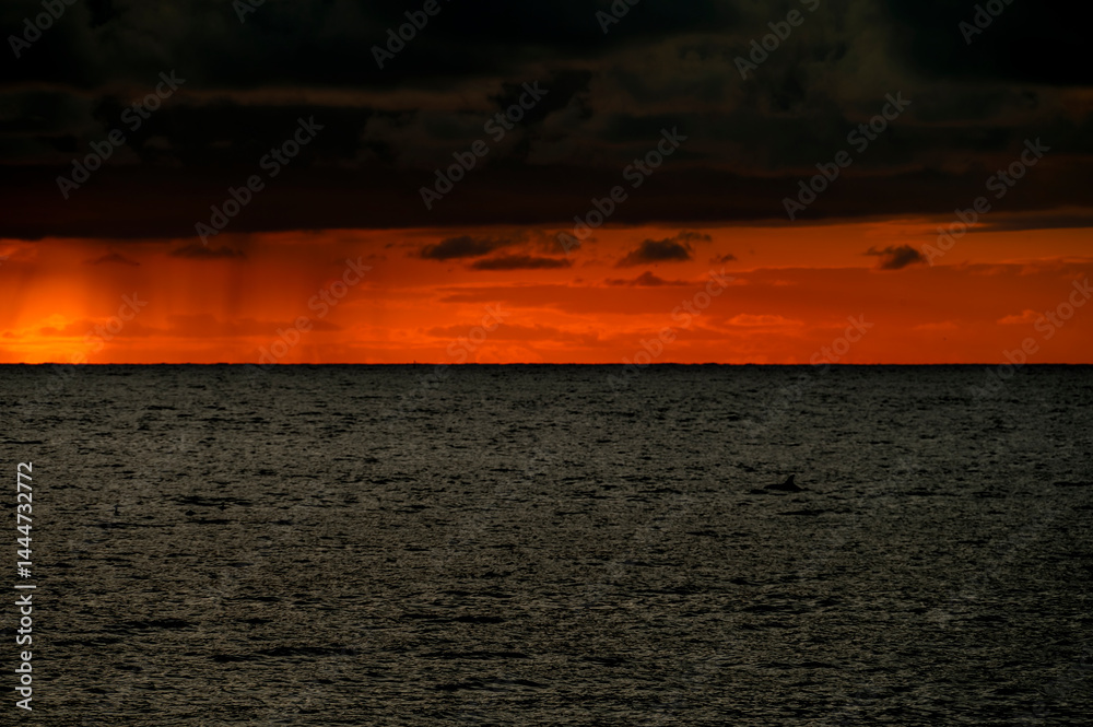 Very moody and dramatic sky over the cloudy ocean horizon, with strong orange, sunbeams and traces of lingering storm cells