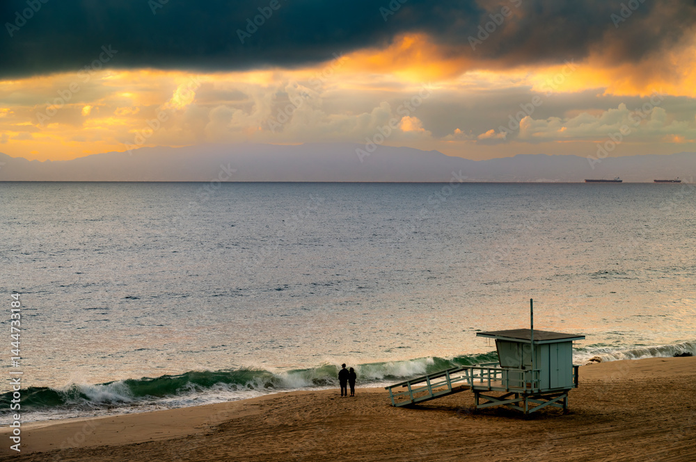 Couple stands on beach next to lifeguard tower, watching the waves right after a storm cell passes