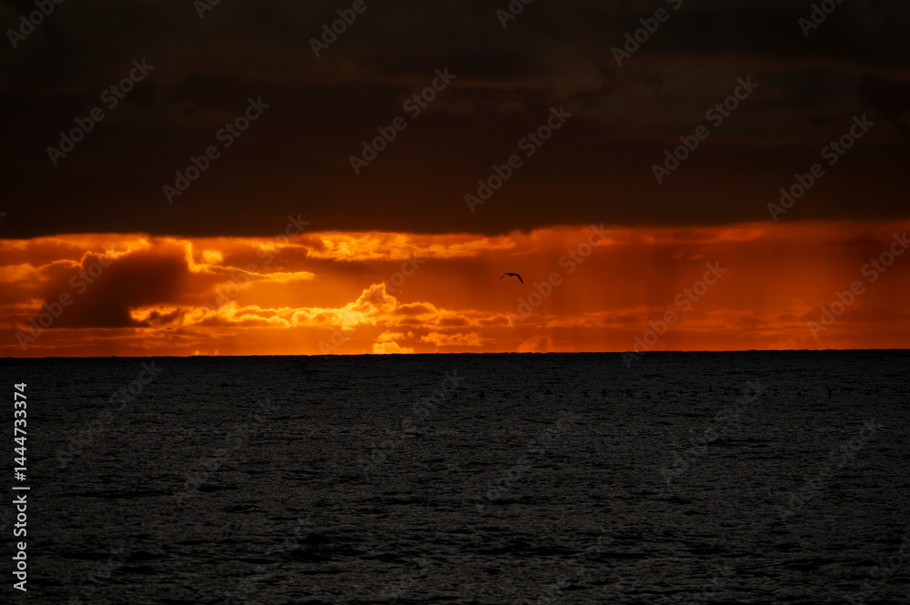 Very moody and dramatic sky over the cloudy ocean horizon, with strong orange, sunbeams and traces of lingering storm cells