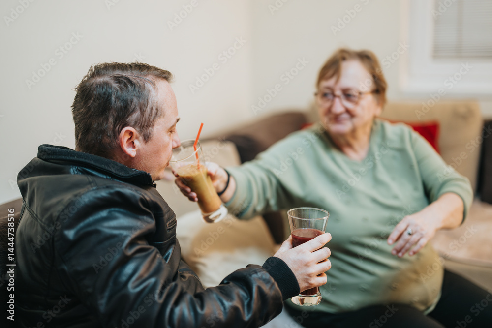 A senior woman and a younger man sharing a friendly moment while drinking beverages in a cozy indoor setting, symbolizing companionship, care, and mutual understanding.