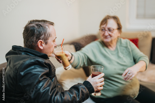 Obraz na płótnie A senior woman and a younger man sharing a friendly moment while drinking beverages in a cozy indoor setting, symbolizing companionship, care, and mutual understanding. w salonie