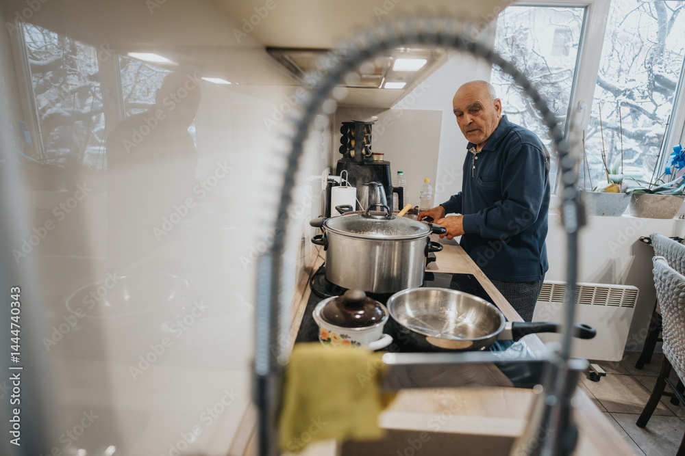 An elderly man preparing food in a modern kitchen, creating a homely atmosphere. Snow visible through the windows emphasizes the warm and cozy indoor setting focused on culinary activity.