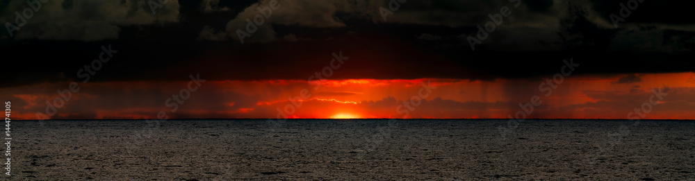 Very moody and dramatic sky over the cloudy ocean horizon, with strong orange, sunbeams and traces of lingering storm cells