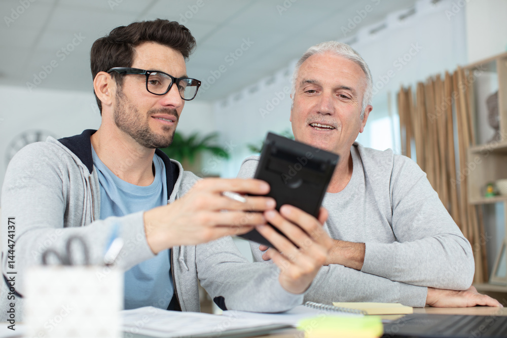 two happy men sitting at table while looking the calculator