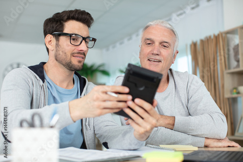 two happy men sitting at table while looking the calculator