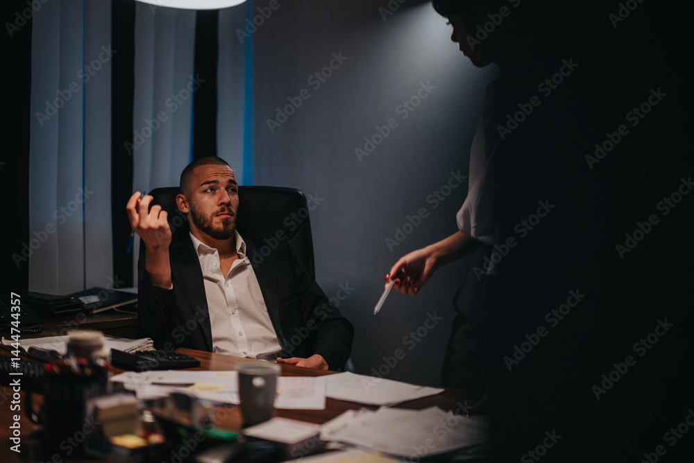 Two professionals converse in a dimly lit office, highlighting teamwork and a focused work environment.