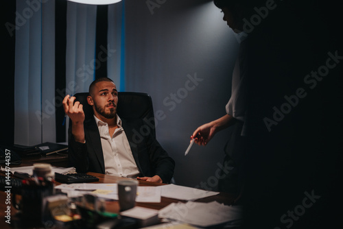 Obraz na płótnie Two professionals converse in a dimly lit office, highlighting teamwork and a focused work environment. w salonie