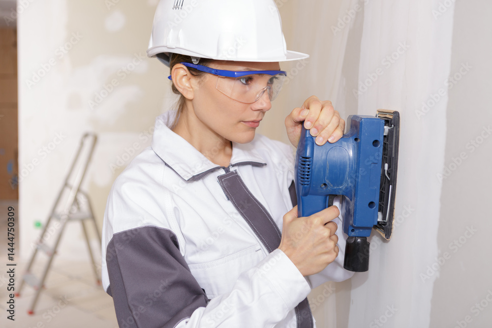 portrait of female contractor using sander on plasterboard wall