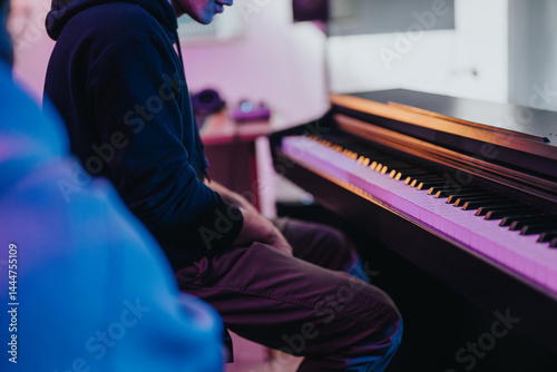 Obraz na płótnie A musician immersed in music creation, playing the piano amidst colorful studio lighting. Capturing the essence of creativity, focus, and artistic expression in a modern music production setting. w salonie