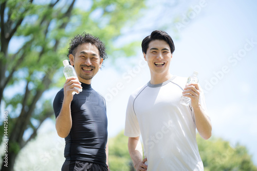 青空の中2人でスポーツする爽やかな男性2人のカメラ目線　ペットボトル夏の水分補給のイメージ