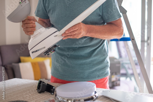Senior man works installing a paddle fan on the ceiling at home, home improvement and DIY concept