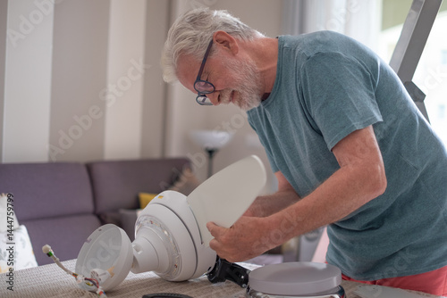 Senior man works installing a paddle fan on the ceiling at home, home improvement and DIY concept