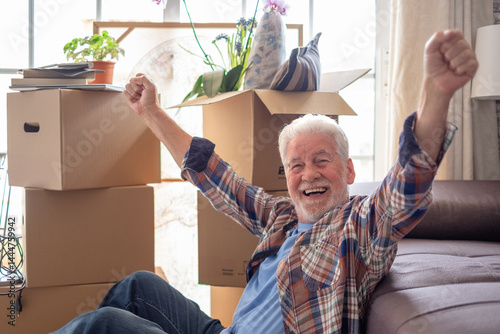 Happy senior man involved in moving house sitting among cardboard boxes having a pause, concept of relocating, retirement, new life, buying, renting, apartment, house