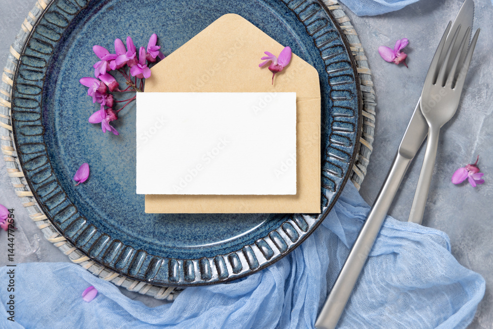 Wedding table place with a card over envelope near fabric and purple flowers top view, mockup