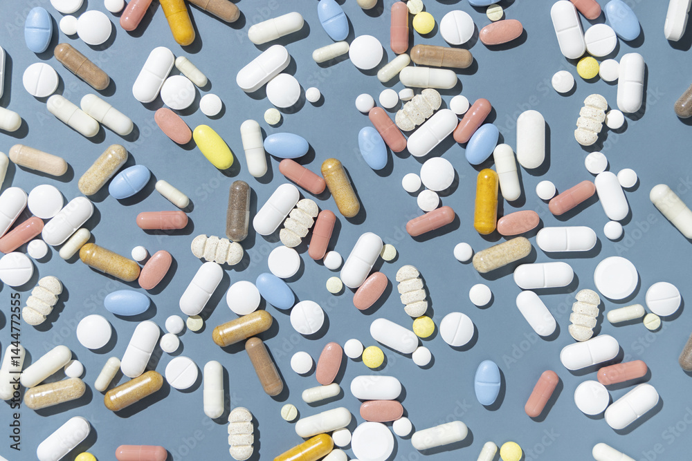 Pile of mixed white, yellow and blue medical capsules and pills on blue top view