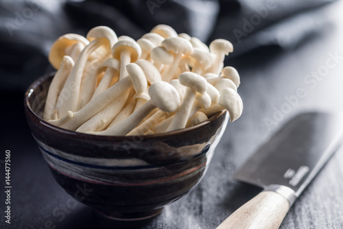 Raw white shimeji mushrooms in bowl on black table.