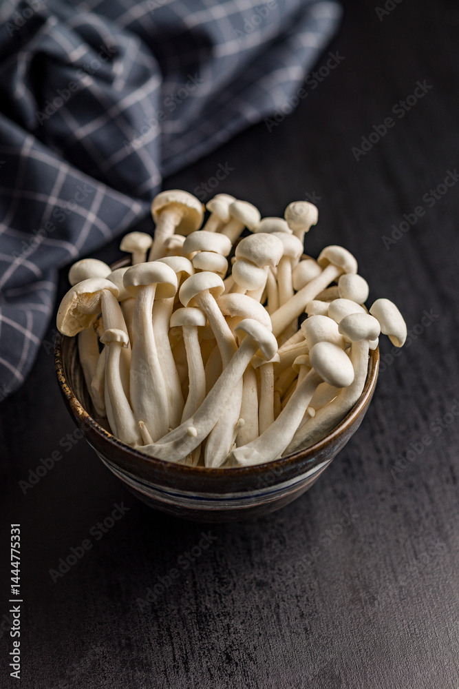 Raw white shimeji mushrooms in bowl on black table.