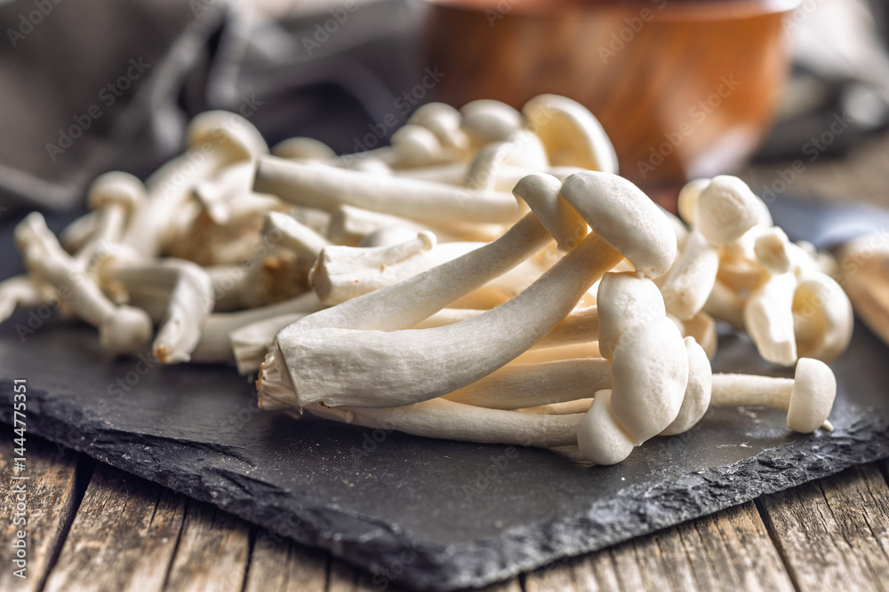 Raw white shimeji mushrooms on cutting board.
